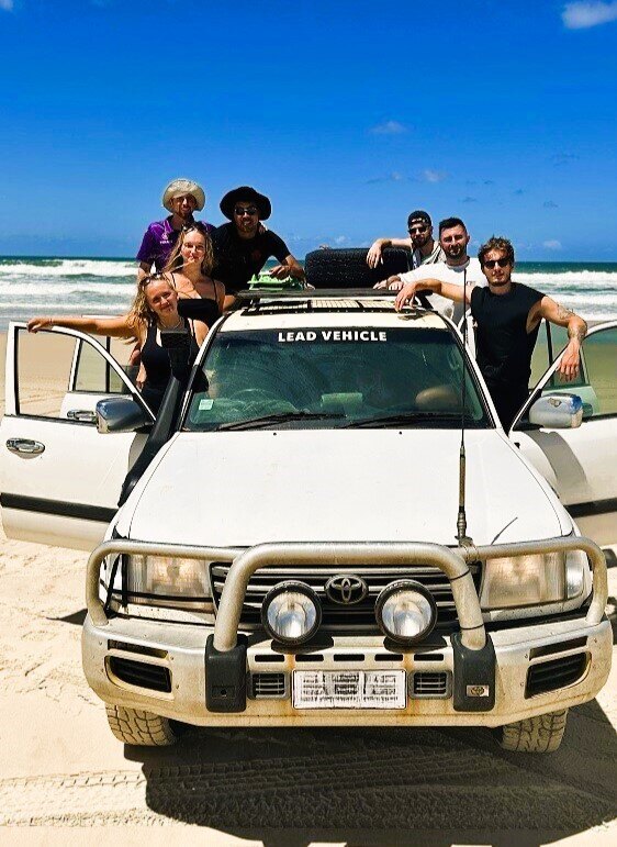 Ein Foto von Personen die an einem Geländewagen auf einem Strand stehen.